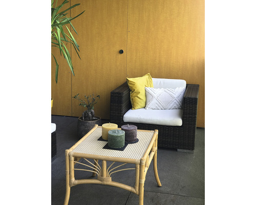 Szene mit Rattan-Sitzmöbeln, Tisch und drei Stumpenkerzen im Außenbereich