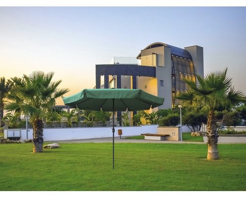 Grüner Sonnenschirm auf einer Rasenfläche vor einem modernen Gebäude und Palmen