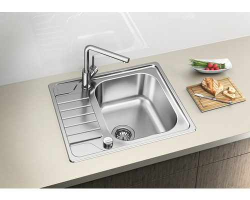 Edelstahlspüle mit Abtropffläche und Küchenarmatur auf einer Arbeitsplatte mit Lebensmitteln