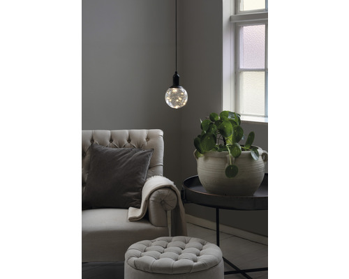 Wohnzimmer mit Sessel, Fußhocker, Tischleuchte und Zimmerpflanze