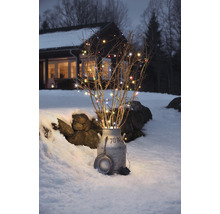 Dekorative Lichterkette mit Zweigen in einer Milchkanne im Schnee vor einem Haus