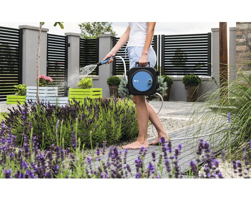 Eine Frau gießt mit einer Gartenschlauchbox Pflanzen im Garten.