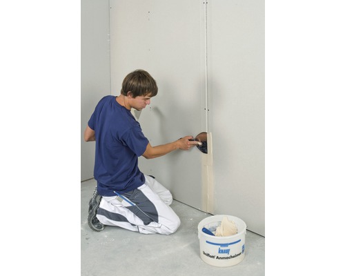 Ein Mann verspachtelt eine Gipskartonwand mit Spachtelmasse in einem Innenraum.