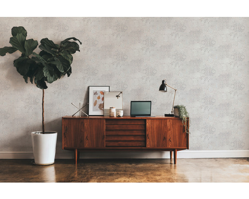 Wohnraum mit gemusterter Tapete, Holzkommode, Zimmerpflanze und Schreibtischlampe