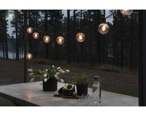 Szene mit einer Lichterkette über einem Tisch mit Dekoration im Freien