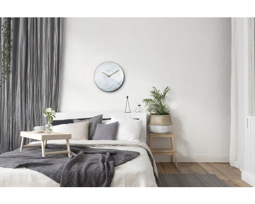 Helles Schlafzimmer mit Bett, Tisch, Pflanze und runder Wanduhr