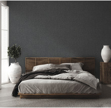 Schlafzimmer mit Bett, Holzkopfteil, Pflanze im Topf und Vase auf einem Holzsockel vor einer strukturierten Wand