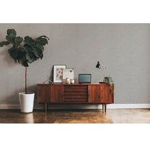 Wohnzimmer mit grauer Strukturtapete, Holzkommode, Zimmerpflanze und Schreibtischlampe.