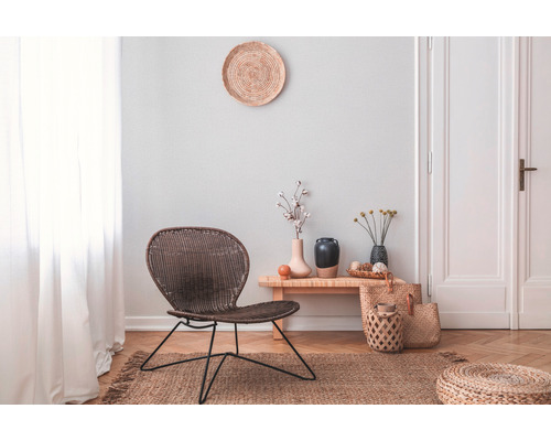 Wohnzimmer mit Rattansessel, Tisch und Dekorationen auf einem Naturfaserteppich