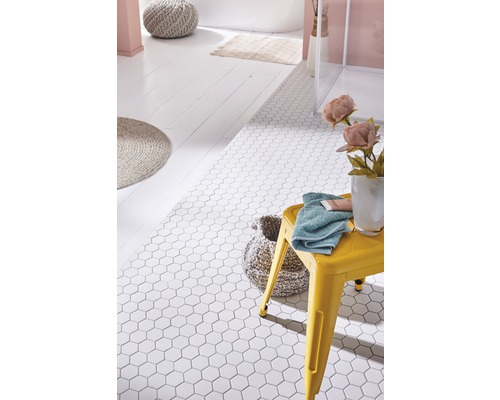 Badezimmer mit weißen, sechseckigen Bodenfliesen, gelbem Hocker, Handtuch und Badezimmeraccessoires.