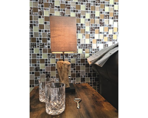 Dekorativer Tisch mit Lampe, zwei Gläsern und Flaschenöffner vor Mosaikwand