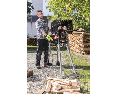 Ein Mann bedient eine Brennholzsäge zum Zuschneiden von Holz im Freien.