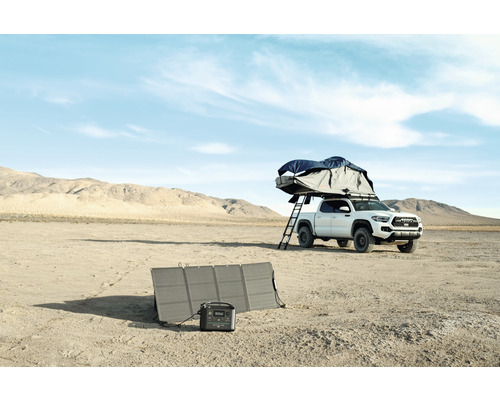 Campingausrüstung mit Solarmodul und tragbarer Powerstation neben einem Pickup mit Dachzelt in der Wüste
