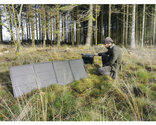Mann hockt im Wald und bedient ein Solarmodul zum Aufladen eines Generators
