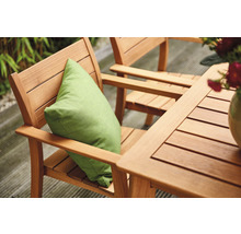 Gartenszene mit Holztisch und Stühlen, einem grünen Kissen und Blumen in einer Vase.