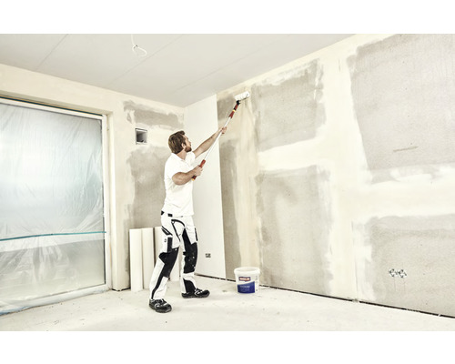 Ein Mann benutzt eine Farbwalze an einer Wand in einem Raum, der renoviert wird.