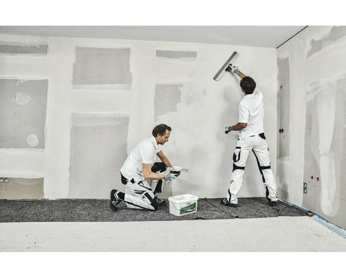 Zwei Handwerker spachteln eine Wand in einem Raum.