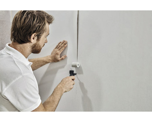 Mann verklebt Tapete mit Andrückroller an der Wand