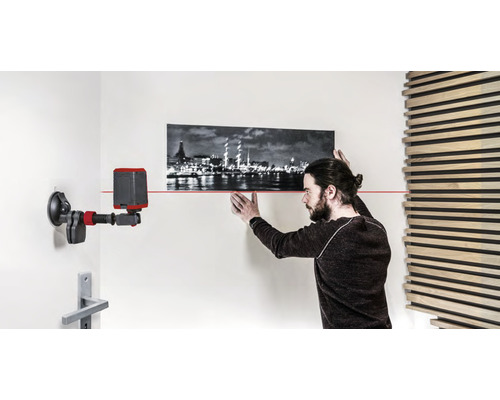Mann richt Bild mit Laser-Wasserwaage an der Wand aus.