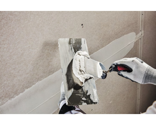 Eine Person verspachtelt eine Wand mit einem Spachtel.