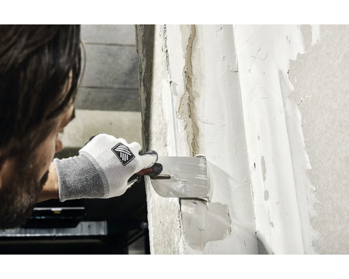 Mann verspachtelt eine Wand mit einem Spachtel.