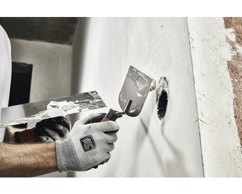 Handwerker verspachtelt eine Wand mit zwei Spachteln