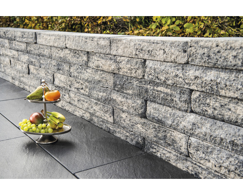 Mauer aus grauen Steinen mit Obstschale auf dunklen Bodenplatten