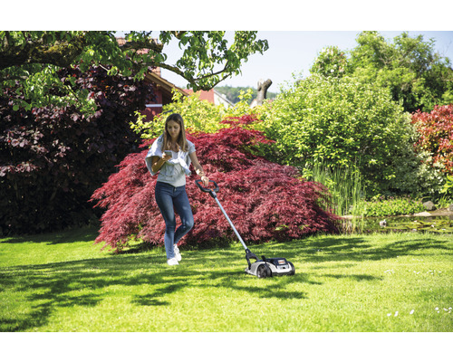 Frau bedient einen Rasenmäher auf einem Rasen im Garten.