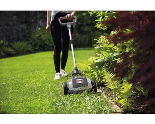 Gartenbesitzerin arbeitet mit einem Rasenkantenschneider im Garten.
