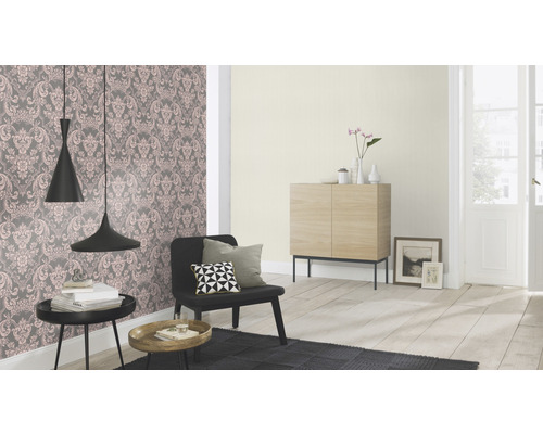 Wohnzimmer mit floral gemusterter Tapete, Sessel, Beistelltischen und Holzschrank