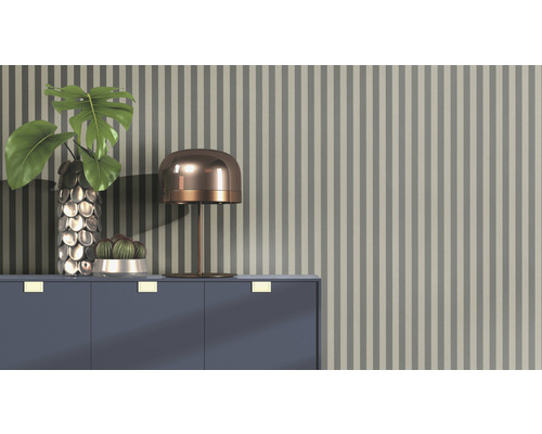 Dekoratives Arrangement mit Tischlampe, Vase, Pflanze und Kaktus auf einem Schrank vor einer gestreiften Tapete.