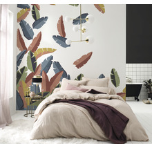 Schlafzimmer mit Bett vor einer Wand mit tropischen Blättern, einer Lampe und einem Badezimmer mit Badewanne.