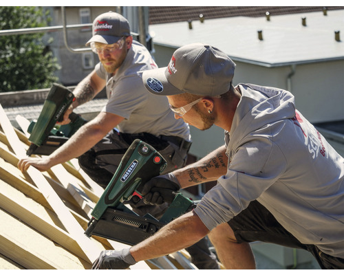 Zwei Handwerker befestigen Dachlatten mit einem Druckluftnagler auf einem Dach.