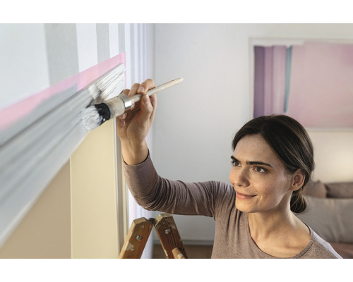 Frau streicht eine Wand mit einem Pinsel und Farbe.