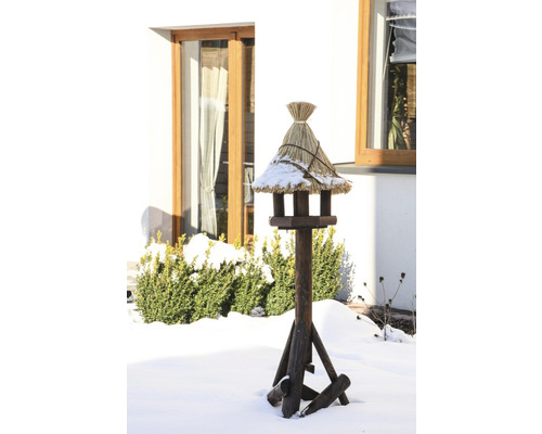 Vogelhaus aus Holz mit Strohdach im verschneiten Garten