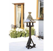 Vogelhaus mit Strohdach auf einem Holzständer im verschneiten Garten.