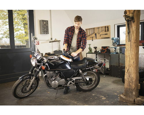 Mann poliert Motorrad mit Poliermaschine in Werkstatt