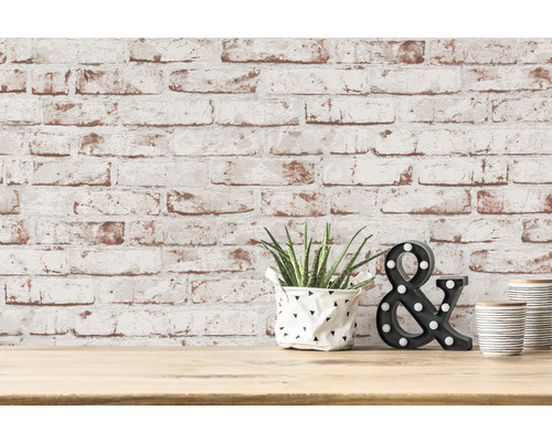 Dekorative Szene mit Pflanze, Ampersand und gestreiftem Behälter vor einer Backsteinmauer