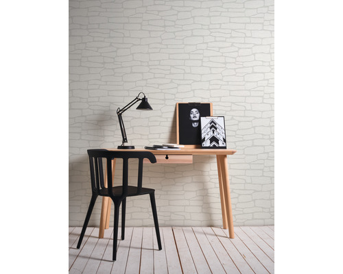 Szene mit Schreibtisch, Stuhl, Schreibtischlampe und einer Wand mit Steinmuster Tapete.