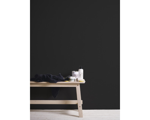 Schwarze Wandfarbe hinter einem Holztisch mit Badartikeln und Handtuch.