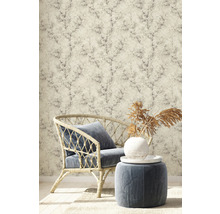 Szene mit Rattansessel, Hocker und Tapete mit Pflanzenmuster für ein stilvolles Interieur