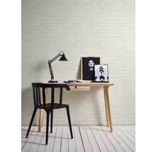 Schreibtisch mit Lampe, Stuhl und dekorativen Bildern vor einer Backsteinmauer