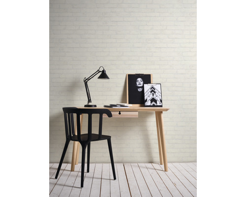 Schreibtisch mit Lampe, Stuhl und dekorativen Bildern vor einer Backsteinmauer