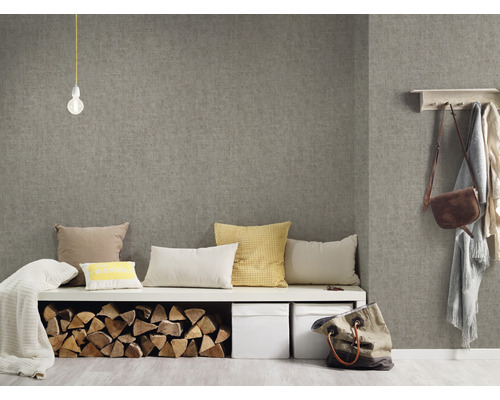 Wohnraum mit grauer Textiltapete, Sitzbank mit Kissen, Holzscheiten und Aufbewahrungsboxen