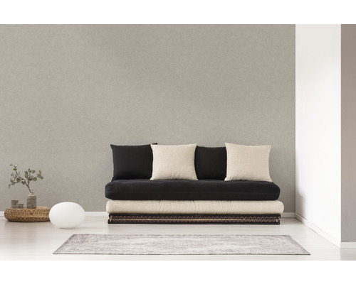 Helles Zimmer mit einer Couch, mehreren Kissen, einem kleinen Tisch, einer Lampe und einem Teppich.