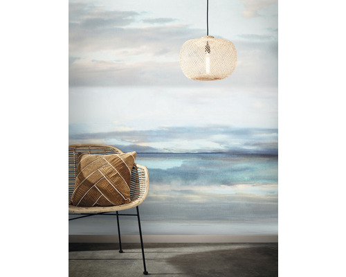 Dekoratives Interieur mit Rattanmöbeln, Textilkissen, Pendelleuchte und Fototapete mit Landschaftsmotiv