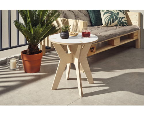 Szene mit einem runden Beistelltisch aus Holz, einem Palettensofa mit Kissen und einer Zimmerpflanze im Topf auf einem Balkon.