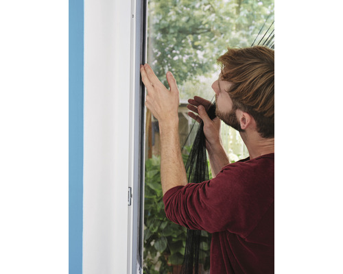 Mann montiert ein Insektenschutzgitter an einem Fensterrahmen.