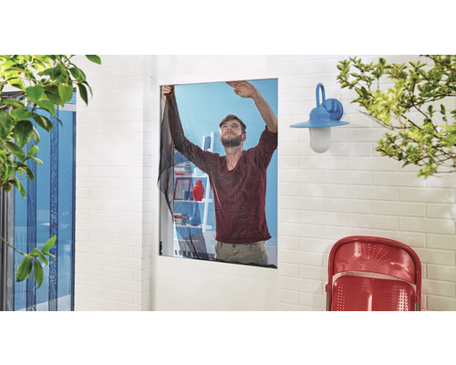 Ein Mann montiert ein Moskitonetz an einem Fenster, um Insekten fernzuhalten.