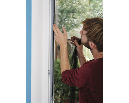 Mann befestigt ein Fliegengitter am Fensterrahmen als Insektenschutz.